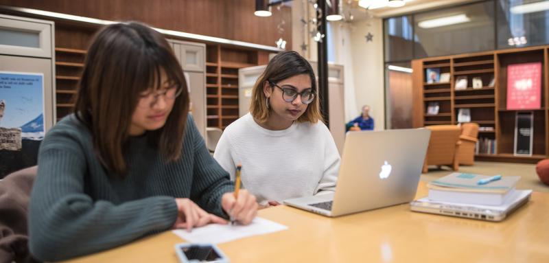 A photo of a student working on a laptop and a student writing.